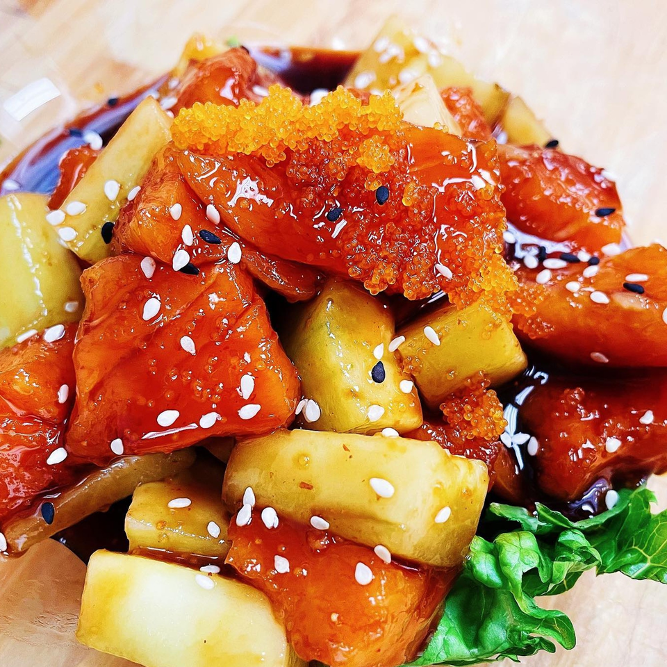 Close-up of a Japanese dish with orange glazed pieces, yellow chunks, orange roe, and sesame seeds.