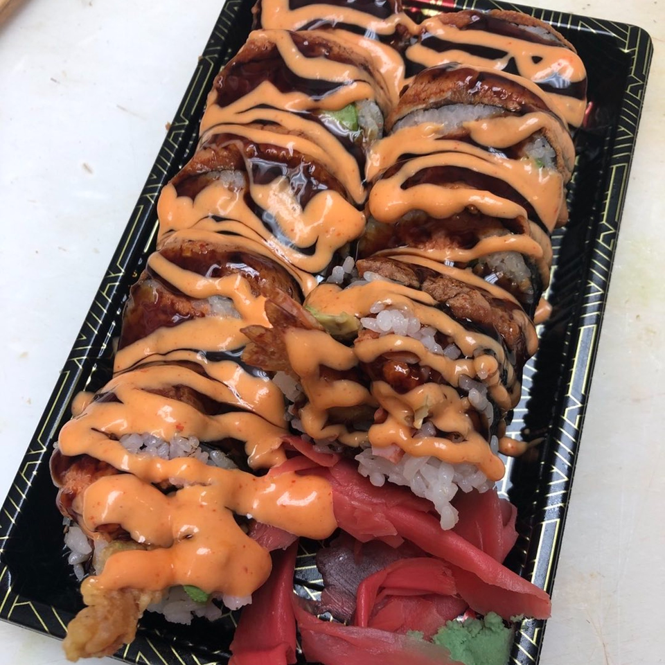 Sushi rolls with dark and orange sauces, pickled ginger, and wasabi in a black tray.