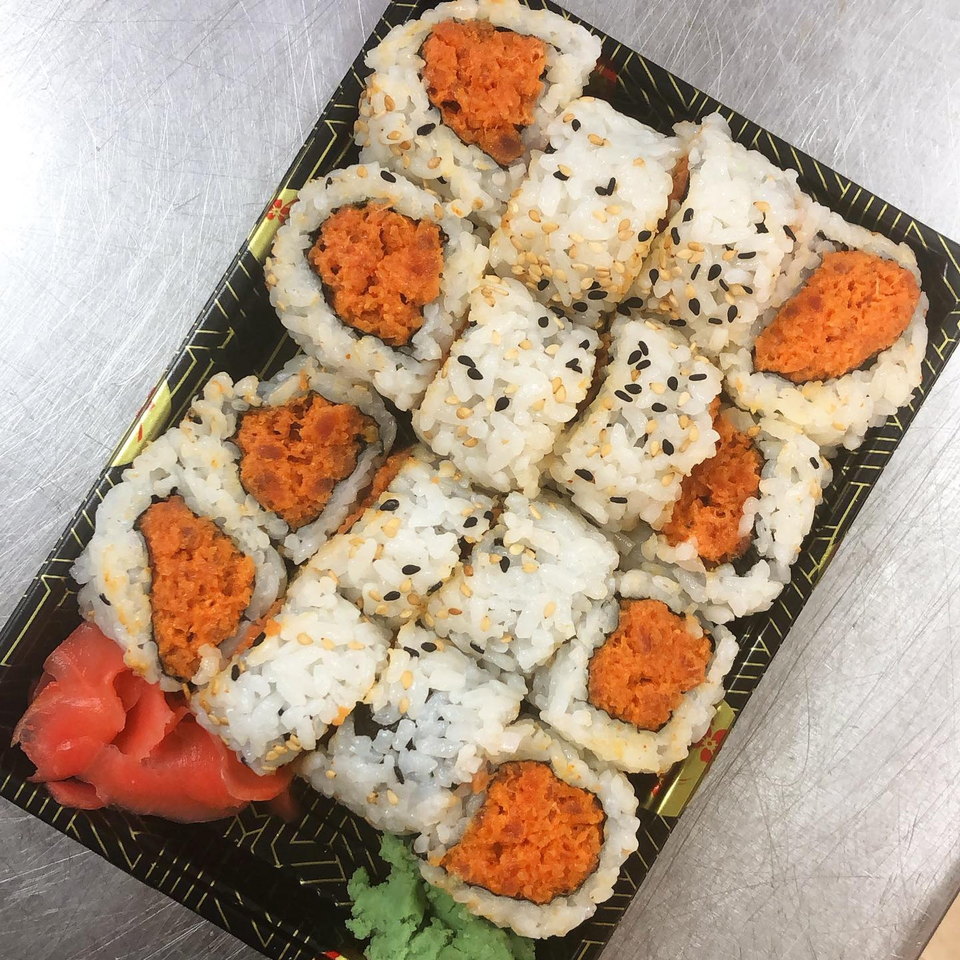 Spicy tuna sushi rolls with white and black sesame seeds, ginger, and wasabi in a black tray.