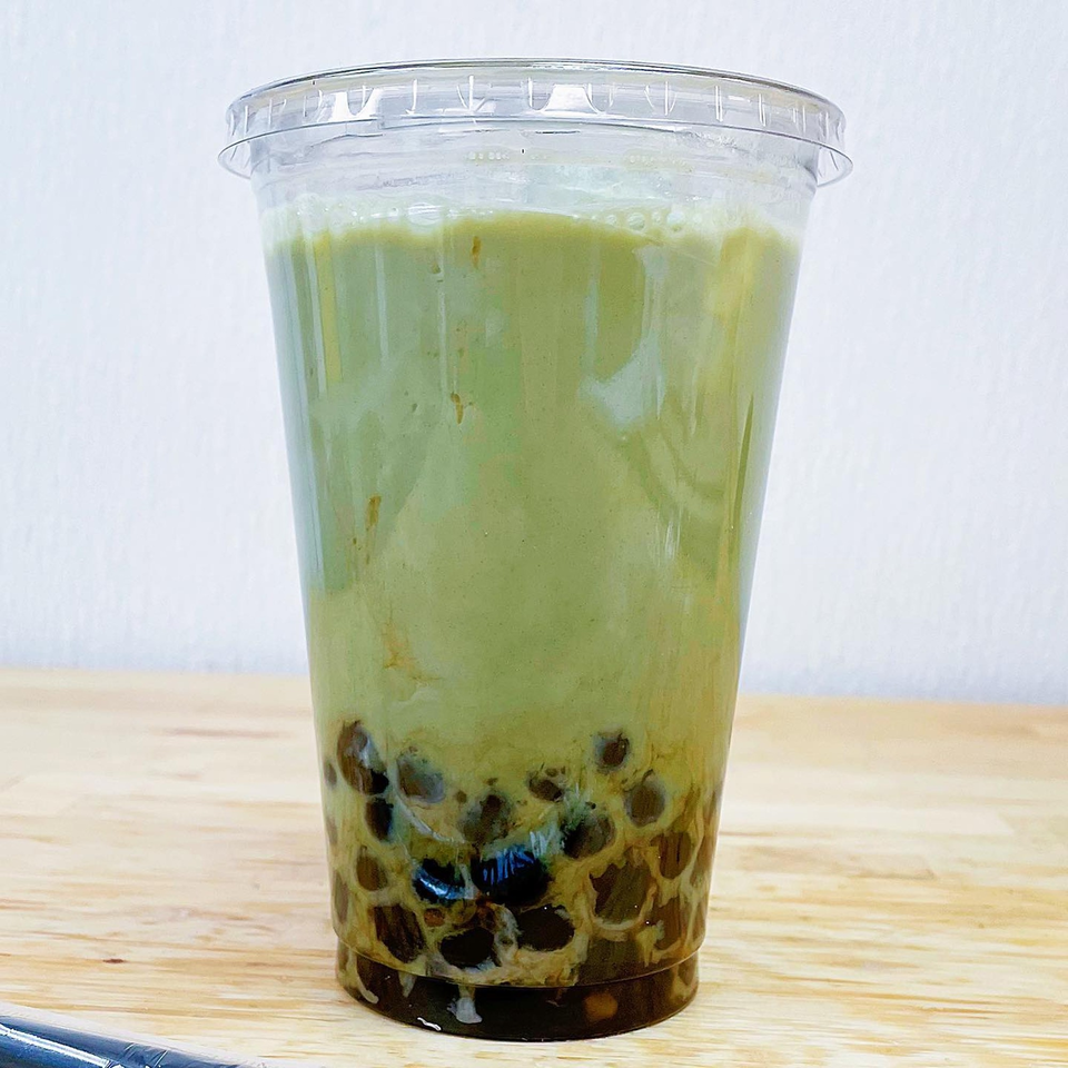 Matcha boba tea in a clear plastic cup on a wooden surface.